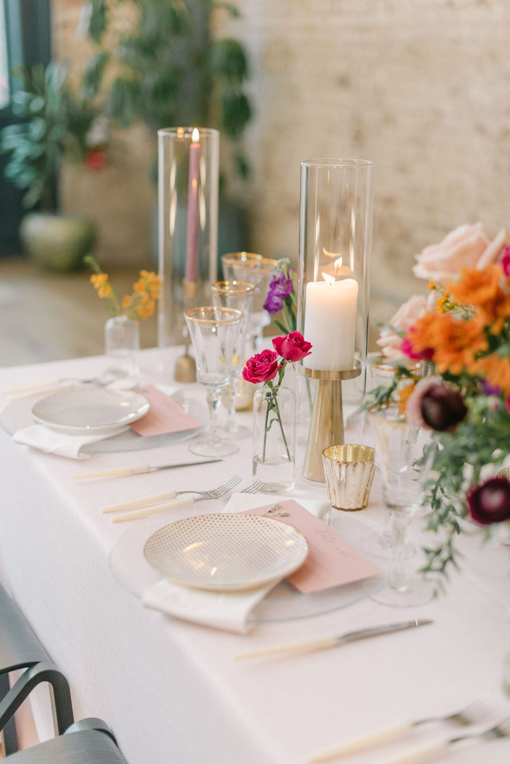 Pink linen with gold plates and white silverware at an elopement reception. Candles and floral adorn the table.