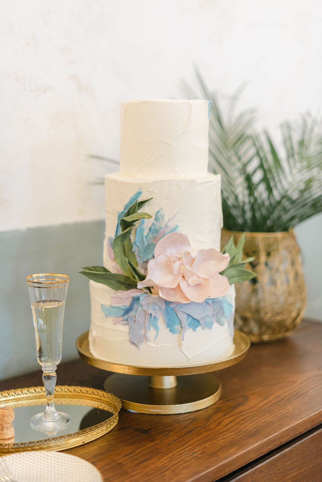 Three tiered wedding cake with pastel florals, sitting on a gold cake stand.