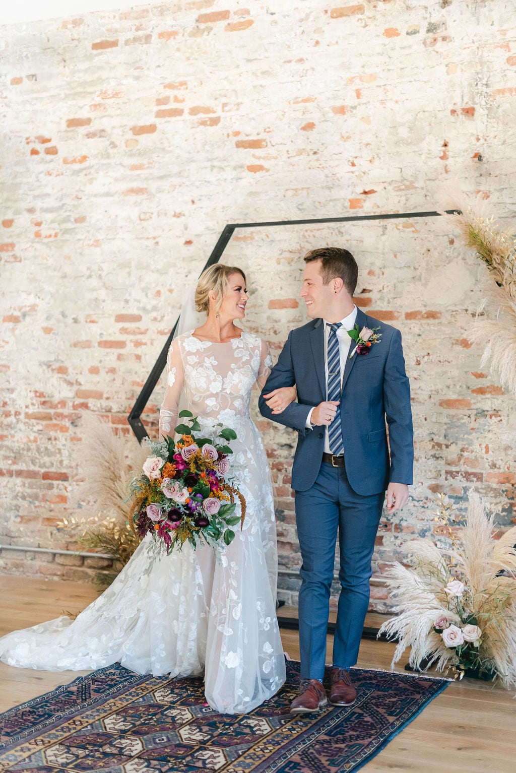Bride and groom smiling at each other after they sealed their first kiss at their wedding ceremony. The backdrop is exposed brick with an octagonal ceremony arbor.